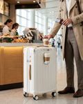 Joyway expandable suitcase with a coffee cup in its built-in holder beside a traveler in an airport concourse